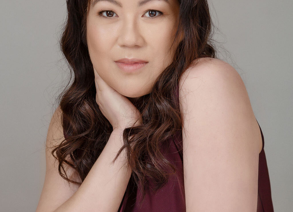 Headshot of a woman of asian heritage with long wavy hair and a soft smile